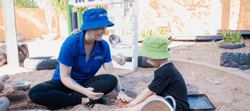 An educator and child play in the sand pit
