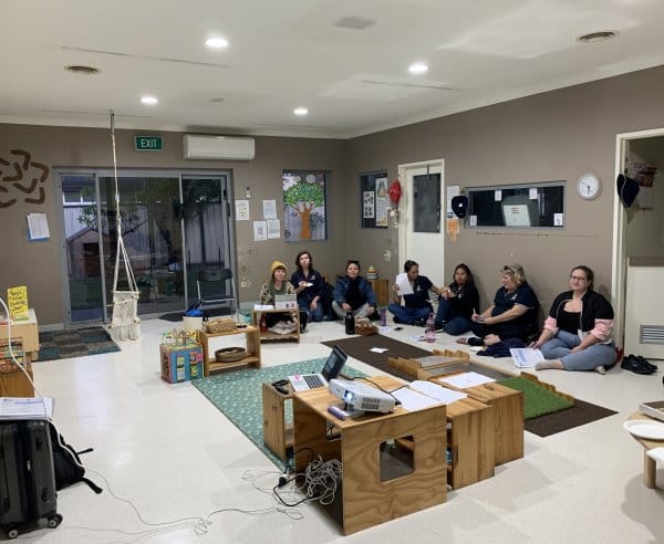 A group of staff members sit down and look at a projector in a daycare room