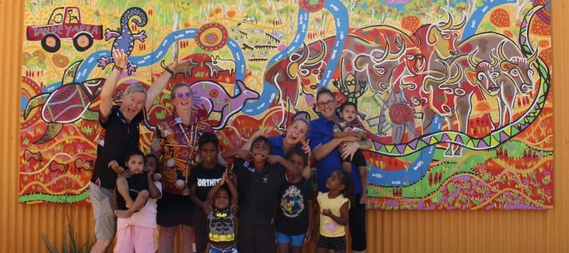 4 staff members and children smile fro a photo in front of artwork
