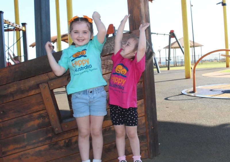 2 kids throw their hands up in the air at the playground
