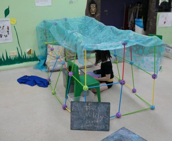 A child builds a fort and reads a book inside it