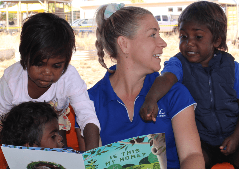 A woman and three kids read a book together